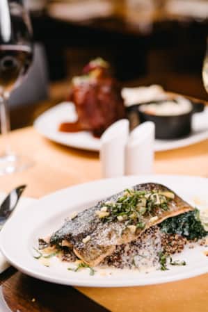 A table set with silverware, wine glasses, and a plate of pan-seared trout.