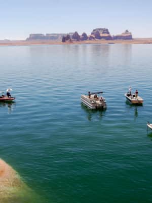 A still lake with rock formations in the background, and boats anchored along the shore.