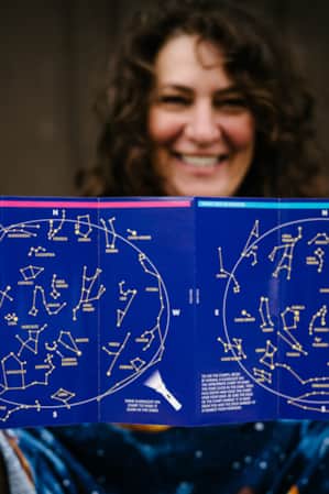 A woman holds a pamphlet with astrological signs on it.