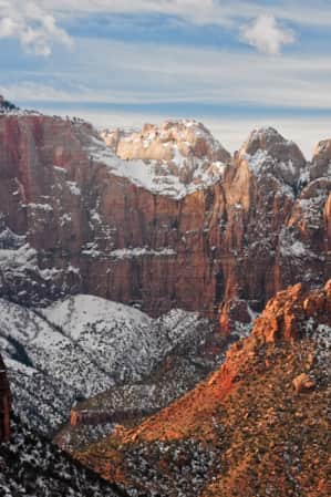 A valley surrounded by massive red rock cliff faces, lightly dusted with snow.