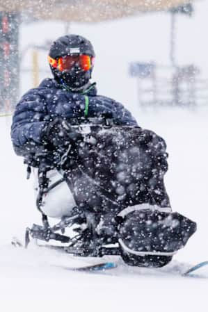 An adaptive skier skiing away from a ski lift during a snowstorm.