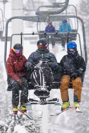 Three skiers sitting on a ski lift during a snowstorm, surrounded by heavy snowfall.