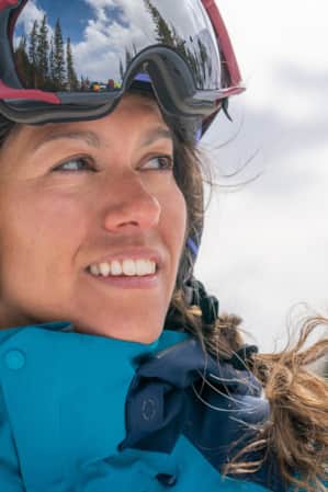 A headshot of a woman in ski clothes and a ski helmet, smiling and glancing to the side.