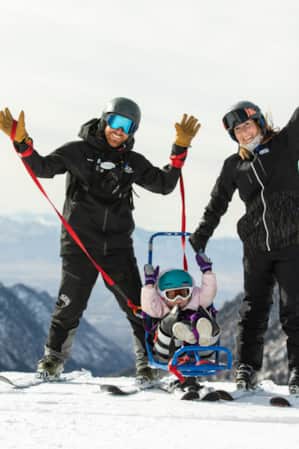 Two skiers smiling with their hands raised in the air, with a small child standing between them.