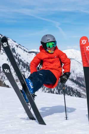 Two kids in ski gear on top of a mountain, propping themselves up with their skis and poles.
