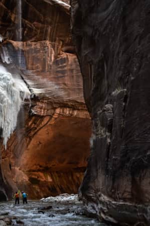 Two hikers in The Narrows looking up and admiring a frozen waterfall.